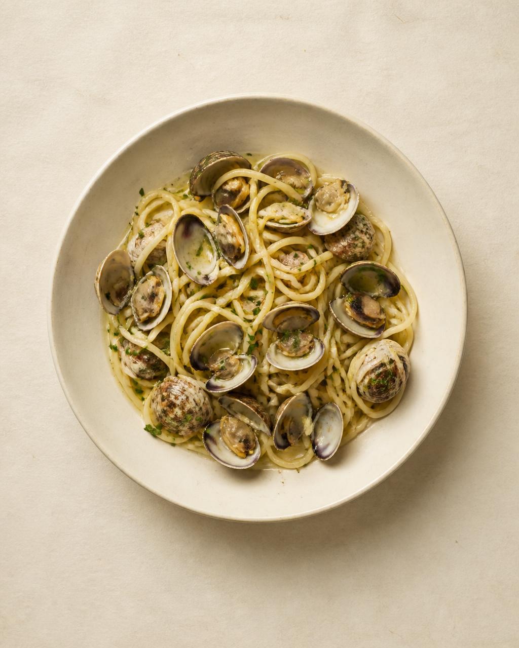 Tagliolini with clams in their shells, parsley and olive oil in a shallow bowl